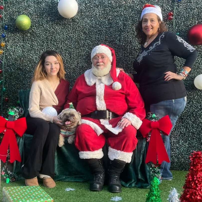 Santa Claus, a woman, and a dog in a festive setting with a green wall and ornaments.