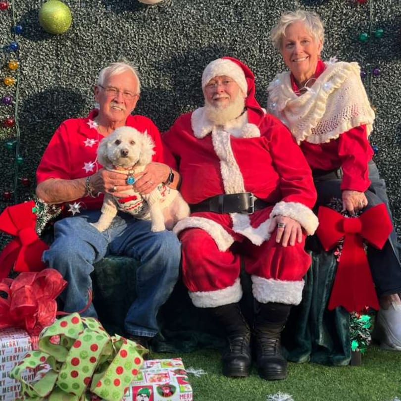 Santa Claus, a man with a dog, and a woman pose for a festive Christmas photo.